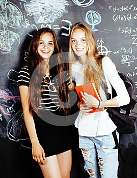 Back to school after summer vacations, two teen real girls in classroom with blackboard painted together, lifestyle