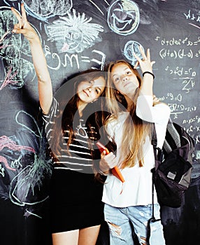 Back to school after summer vacations, two teen real girls in classroom with blackboard painted together, lifestyle