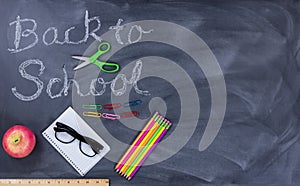 Back to school text on erased chalkboard with student supplies