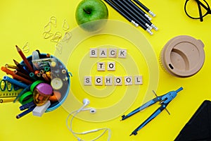 Back to School wooden blocks with school supplies and green apple on yellow desk. Top view, flat lay