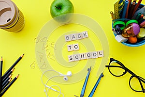 Back to School wooden blocks with school supplies and green apple on yellow desk. Top view, flat lay