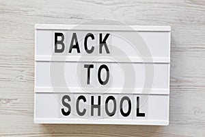 `Back to school` word on lightbox over white wooden surface, from above. Top view