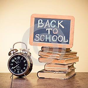 Back to School written on a blackboard, alarm clock, books on wooden table. Vintage style photo