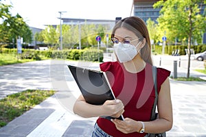 Back to school. Young woman with glasses and FFP2 protective mask review the lesson before entering the school