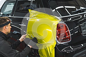 Back and truck of a car during car wrapping process at detailing station. Professional car detailer glueing yellow