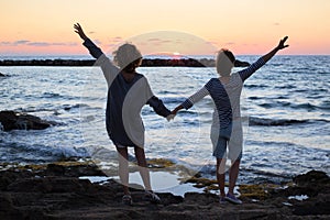 Back view of 2 women holding hands at sunset on sea coast. ocean sky background