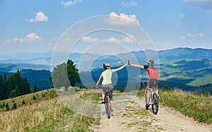 Back view of active couple cyclists in sportswear and helmets cycling down cross country bikes