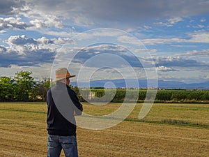 Back view of adult man farmer stand alone and look at sunset or sunrise in sky. Guy stand on wheat field. Ripe harvest time. Sun