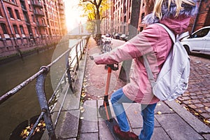 Back view of adult woman tourist with backpack discover Hamburg city on e-scooter. Most famous historic Speicherstadt