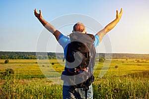Back view of aged man with rucksack in the field with hands lift