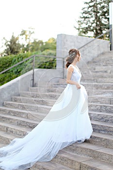 Back view of american bride walking on concrete stairs and wearing white dress.