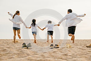 Back view of Asian having family parents with child fun holding hands together running to beach