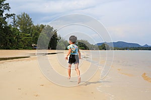 Back view of Asian little boy having fun running on tropical sand beach