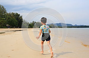 Back view of Asian little boy having fun running on tropical sand beach