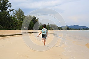 Back view of Asian little boy having fun running on tropical sand beach