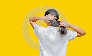 Back view of Asian woman holding damaged hair on yellow background with copy space. Split ends hair problem in woman. Dry and