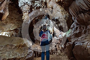 Back view of asian woman traveller walking in the cave to explore cave with stalagmites and stalactites.