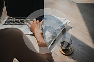 Back view of asian woman using computer, lying on floor while working on laptop with coffee and typing keyboard