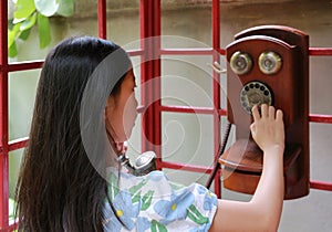Back view of Asian young girl child using dial telephone booth. Kid call on the retro vintage red phone booth