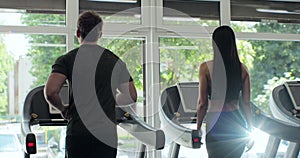 Back view of athletic man and beautiful woman walking on treadmills. Work out in a sport club. Healthclub.