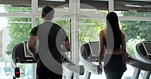Back view of athletic man and beautiful woman walking on treadmills. Work out in a sport club. Healthclub.