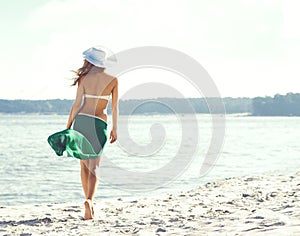 Back view of attractive girl in green silk walking along the sea