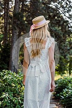 back view of attractive girl in white dress and wicker hat walking