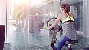 Back view of attractive woman at the gym riding on the spinning bike with huge panoramic window