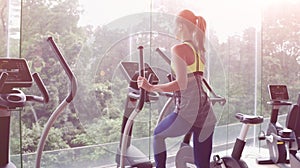 Back view of attractive young woman working out on an elliptical trainer in gym. Panoramic windows