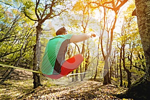 Back view A bearded man in age balances while sitting on a taut slackline in the autumn forest. Outdoor Leisure