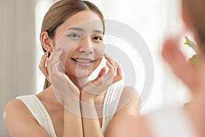 Back view of beautiful Asian young woman looking in the mirror after wake up preparing skin for make up. Healthy female looking