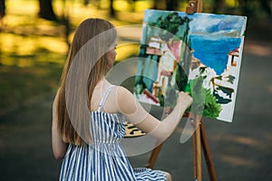 Back view of beautiful blond hair girl drawing a picture in the park