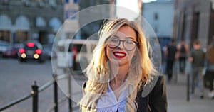 Back view of a beautiful blonde woman in a formal outfit and in glasses walking down the city street, turning to camera