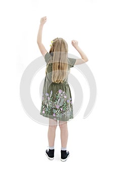 Back view of beautiful little girl in dress looking at wall and holds hand up. young blonde girl standing. Rear view people.