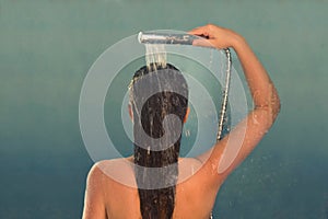 Back view of beautiful naked young woman taking shower in shower cabin.