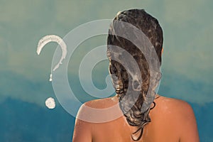 Back view of beautiful naked young woman taking shower in shower cabin. Soap question mark on shower cabin in the bathroom.