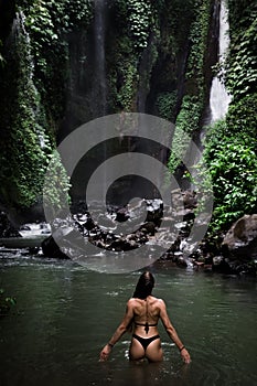 Back view of beautiful woman bathing and relaxing in natural swimming pool before waterfall in natural park on tropical