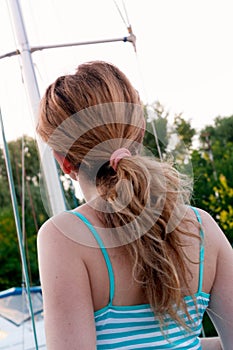 woman in blue top with pony tail looking away in front of sky and green trees in yachts club