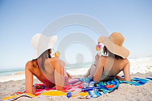 Back view of beautiful women sunbathing while sipping cocktails on the beach
