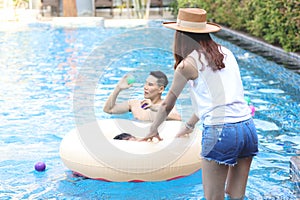 Back view of beautiful young Asian woman in summer hat has a great time at pool party, cheerful female and friend have fun with