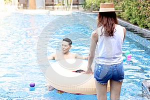 Back view of beautiful young Asian woman in summer hat has a great time at pool party, cheerful female and friend have fun with