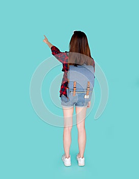 Back view of beautiful young asian woman travel with backpack pointing something isolated on blue background.