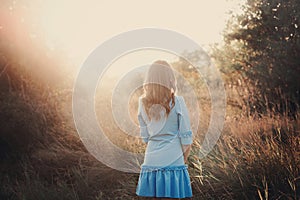 Back view of a beautiful young woman or girl on very green meadow watching the sunset