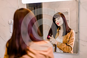 Back view of beautiful young woman in white undershirt and yello shirt, combing her dark red straight hair and smiling