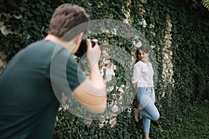 Back view of blurred man taking photos of woman who is posing near wall