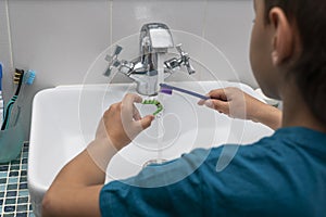 Back view of boy cleaning his dental orthodonic plates with  toothbrush.