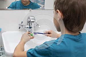 Back view of boy cleaning his dental orthodonic plates with  toothbrush.