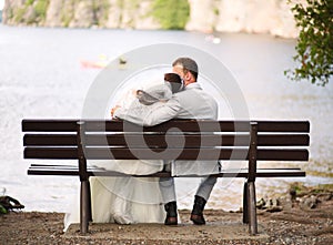 Back view of a bride and groom kissing on a bench near a pond