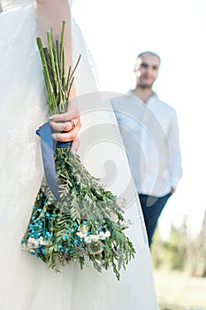 Back view on bride holding rustic wedding bouquet with tourquoise colour details and lens blurred groom on background photo