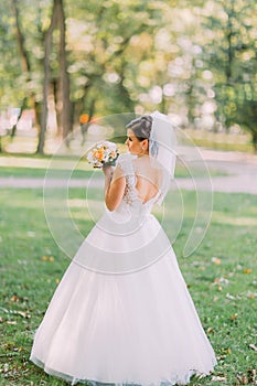 The back view of the bride holding the yellow wedding bouquet at the background of the park.